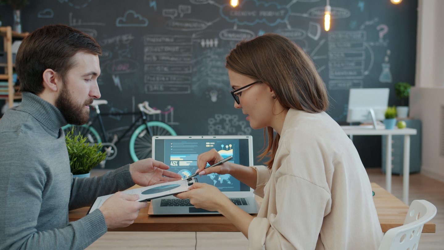 Des professionnels collaborent autour d'un ordinateur portable et de graphiques sur un bureau en bois.