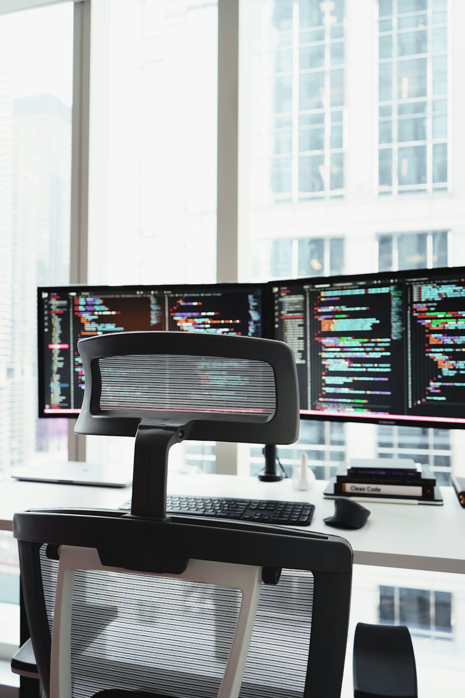 Deux écrans d'ordinateur affichant du code sur un bureau blanc.