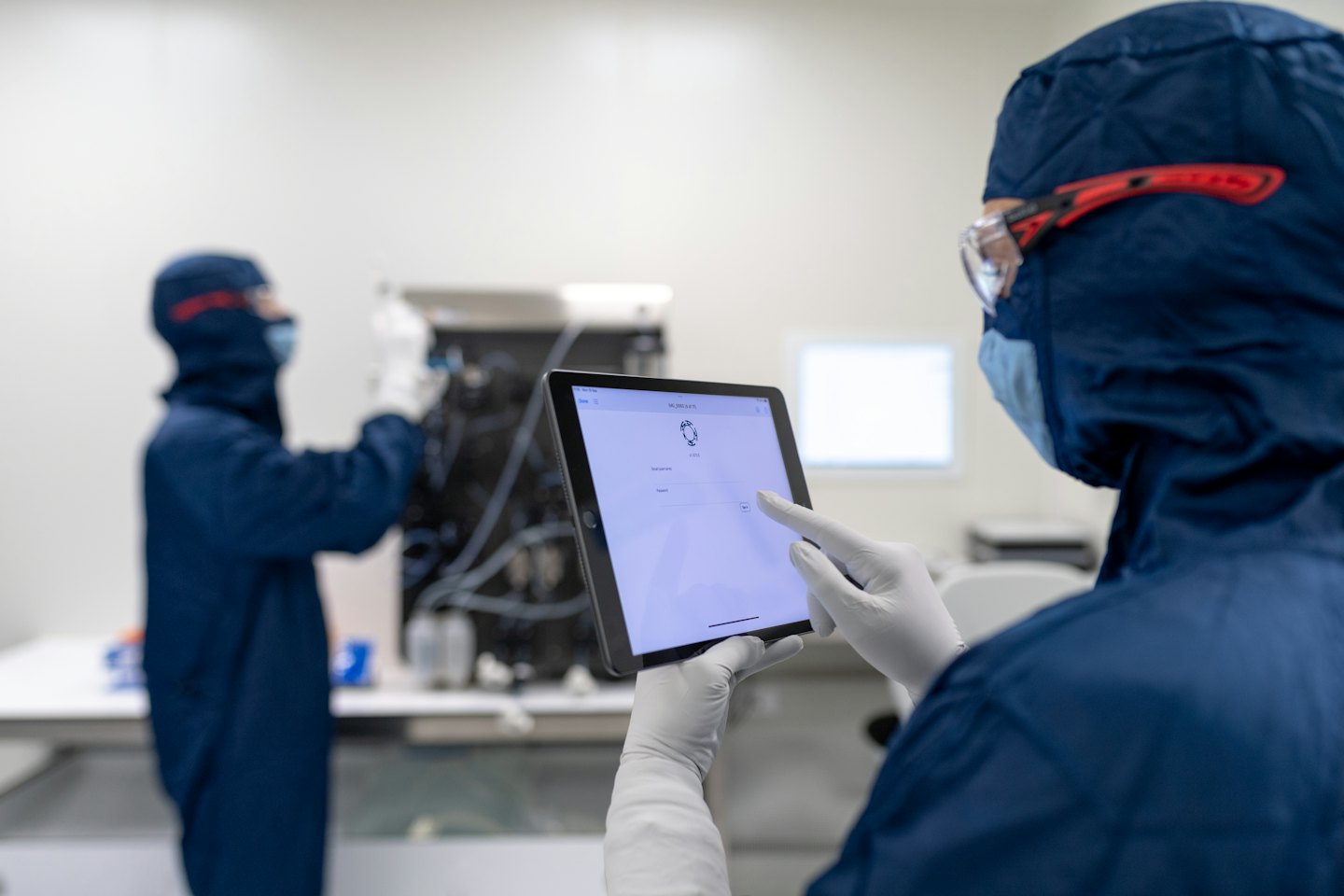 Un travailleur en salle blanche utilise une tablette pour contrôler l'équipement de laboratoire.