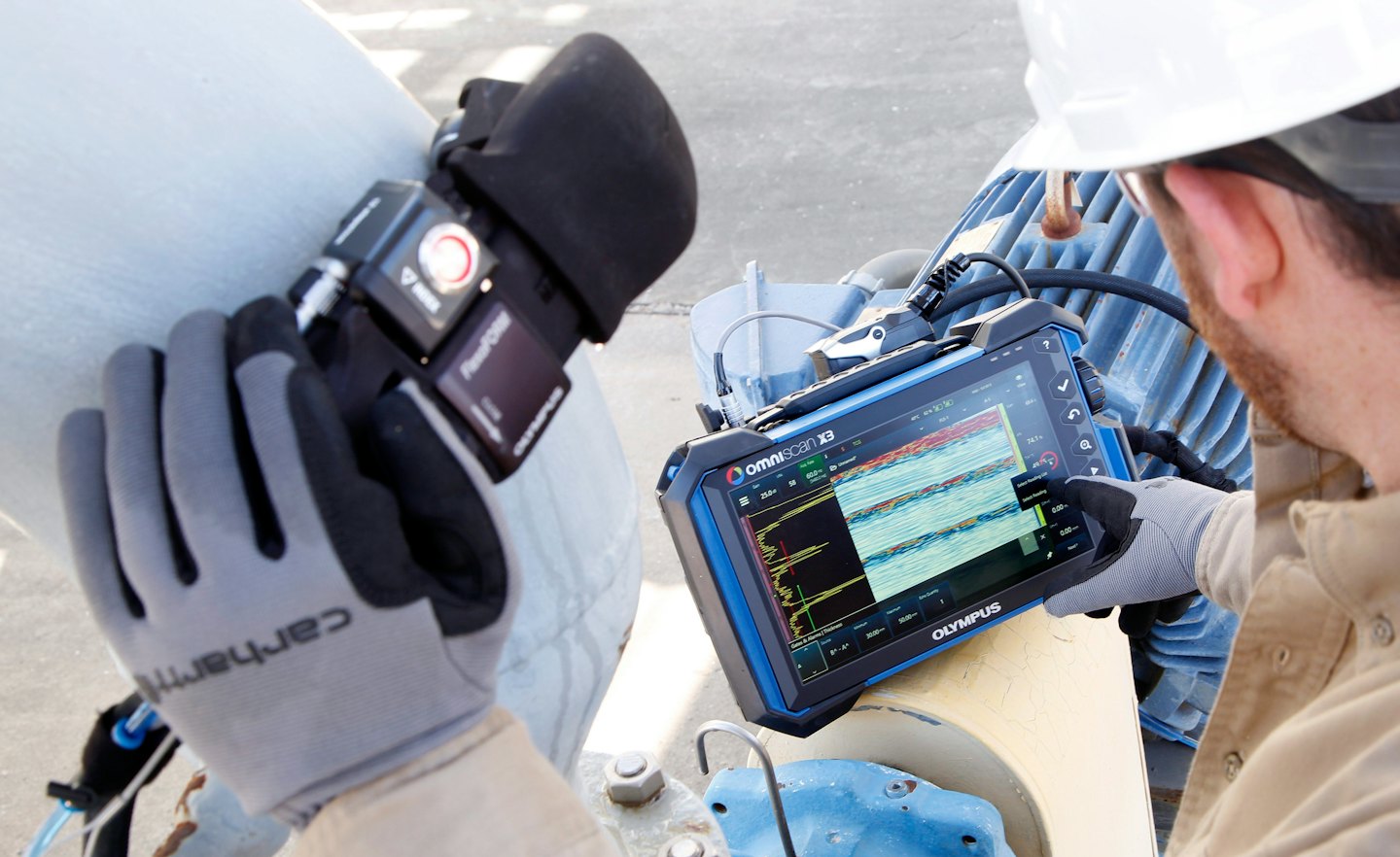 Un technicien utilise un capteur et une tablette pour tester un tuyau industriel.