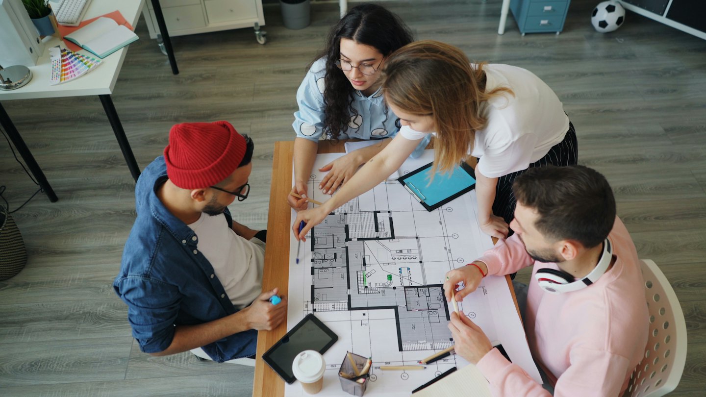 Quatre designers collaborent autour d'une maquette architecturale sur une table.